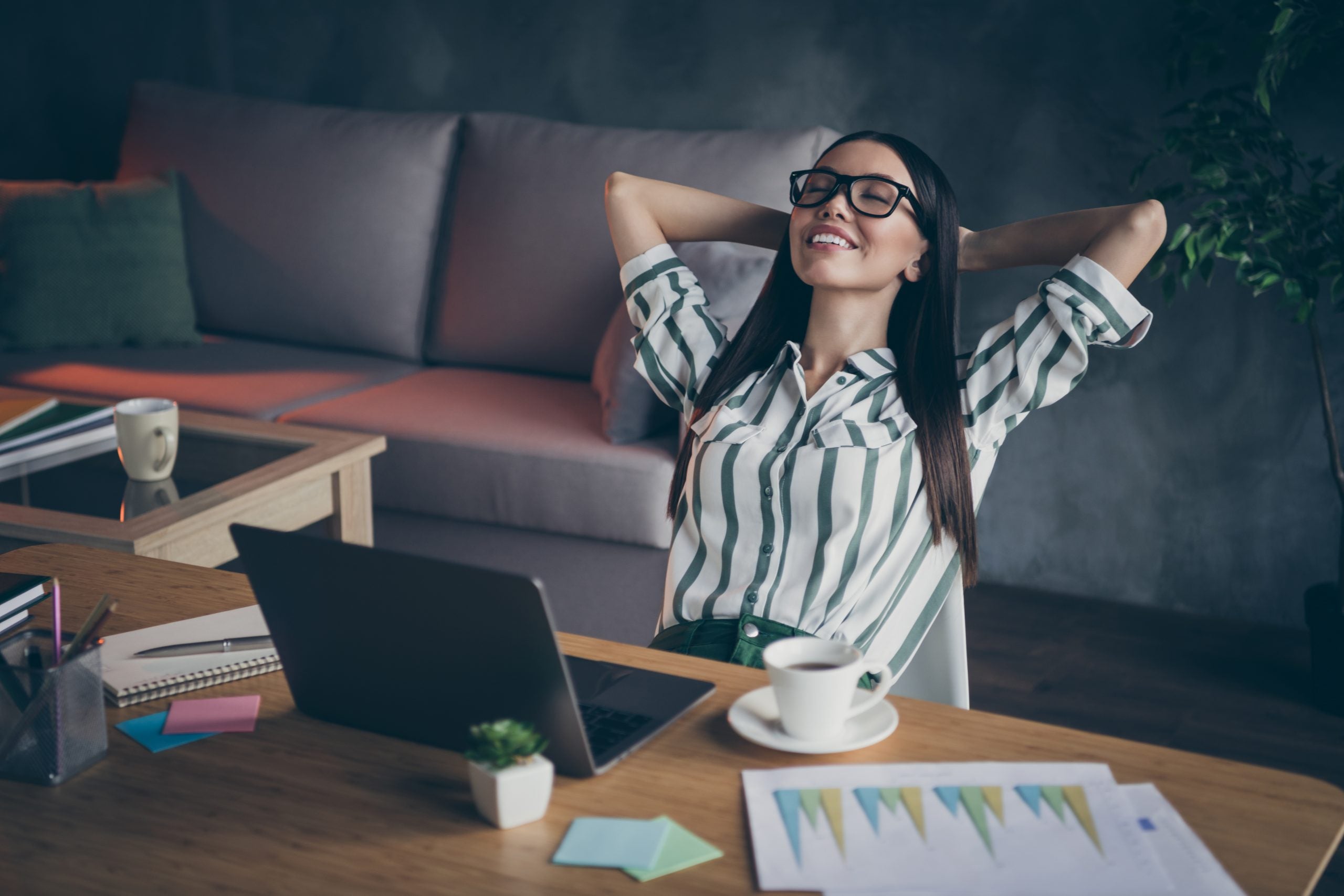 Photo of cheerful relaxing girl having rest at her work place smiling toothily lying on hands behind her head in spectacles